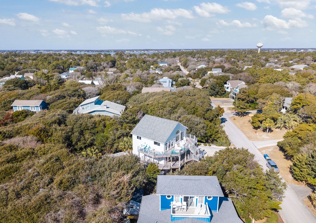 Aerial view of coastal vacation homes nestled among lush trees in a peaceful residential neighborhood near the shore.