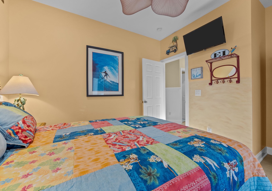 Relax in your colorful bedroom with tropical-themed bedding, wall-mounted TV, and charming surf artwork creating a cheerful coastal atmosphere.