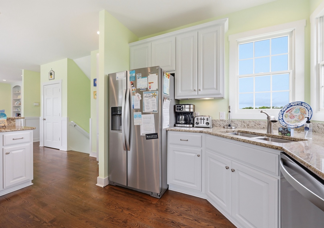 Bright, fully equipped kitchen with granite counters, stainless appliances, and coffee station ready for your morning brew. Large windows flood the space with natural light.