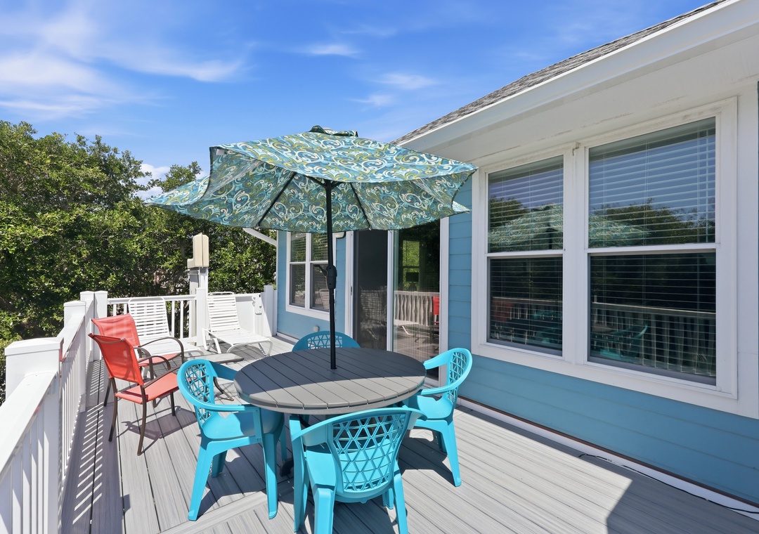 Enjoy morning coffee or evening meals on your private deck, complete with comfortable seating, cheerful turquoise dining set, and a shaded umbrella perfect for sunny afternoons overlooking lush greenery.