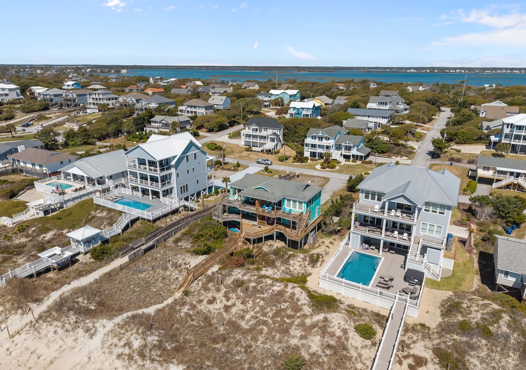 Aerial view of coastal vacation homes with swimming pools nestled among beach community neighborhoods near the sparkling waterfront.