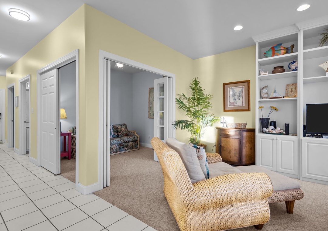 Unwind in your spacious living area with wicker armchairs, entertainment center, and tranquil decor creating the perfect coastal retreat atmosphere.