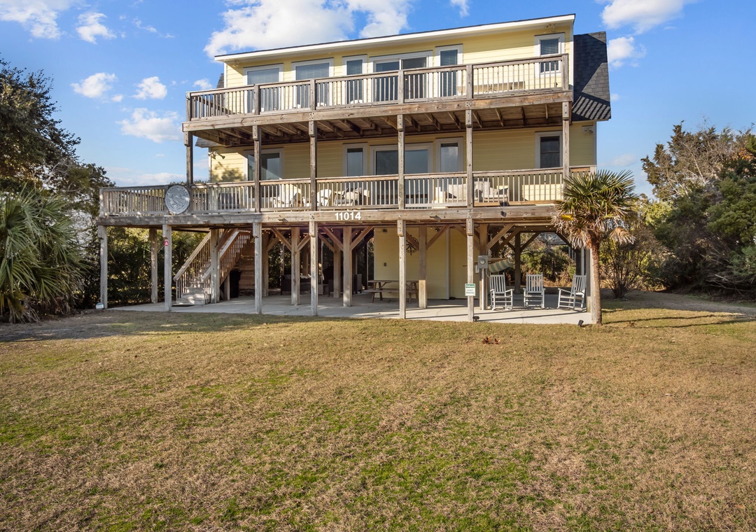 Coastal retreat featuring spacious wraparound decks and elevated beach architecture surrounded by lush landscaping.