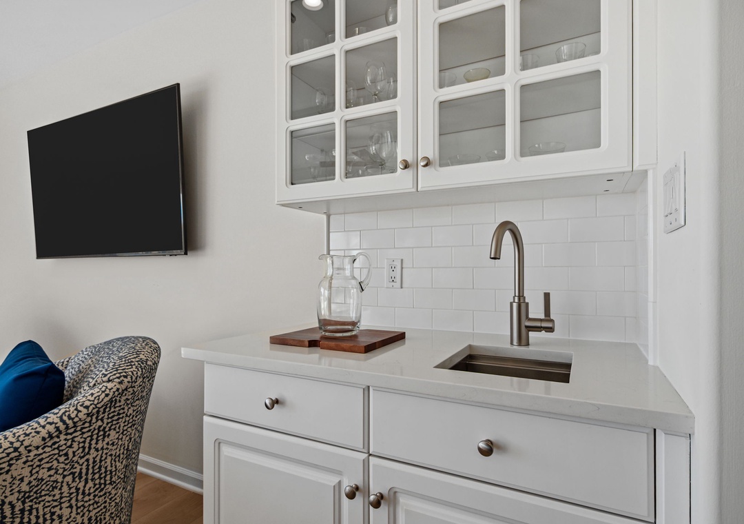 Your elegant wet bar features white cabinetry, subway tile backsplash, and modern appliances for convenient meal prep.