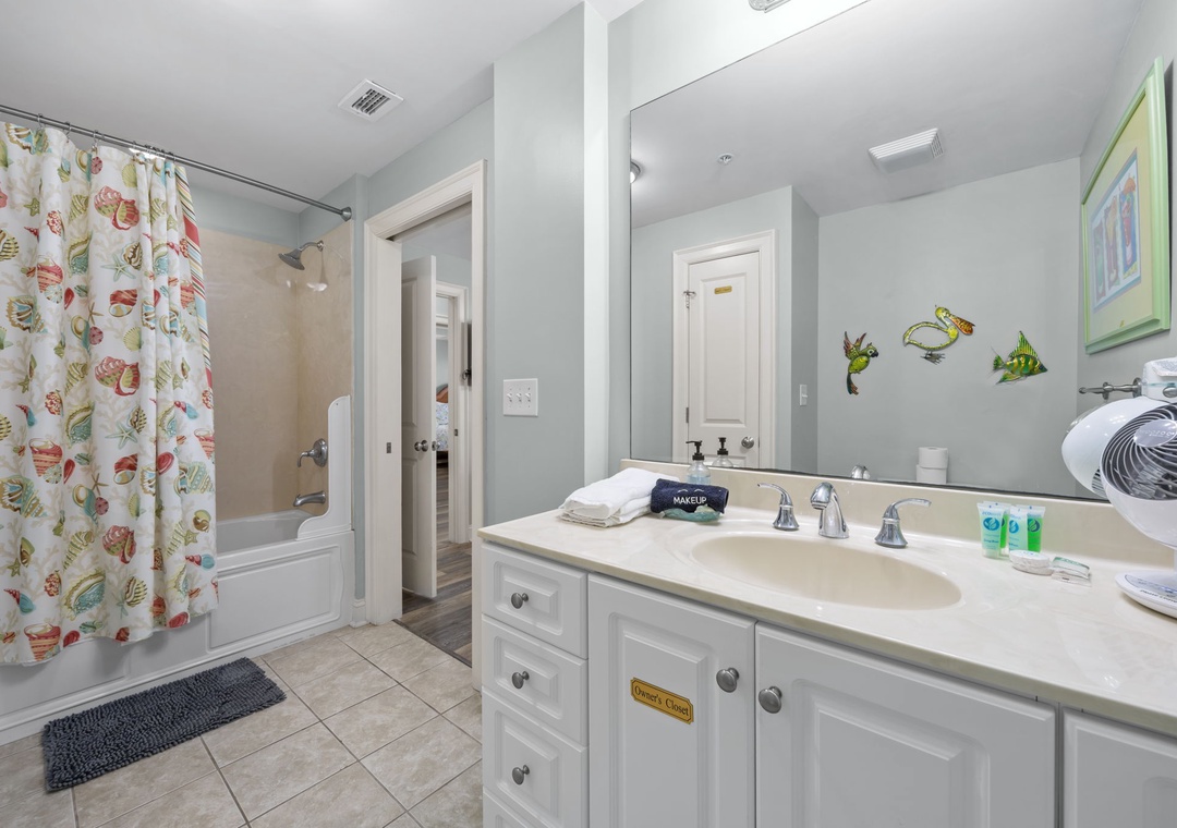Your spacious bathroom features a relaxing tub with tropical fish shower curtain, well-lit vanity with fresh amenities, and thoughtful nautical touches throughout.
