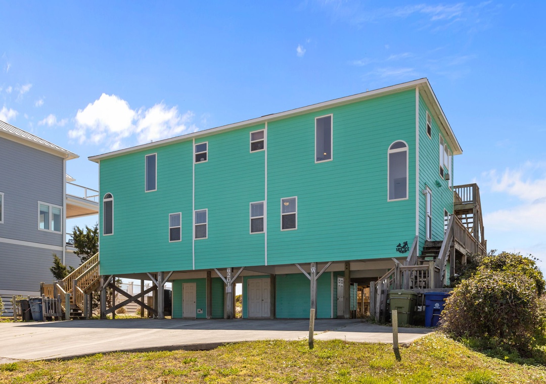 Coastal rental home featuring bright turquoise siding and elevated design, situated in a charming beachside neighborhood.