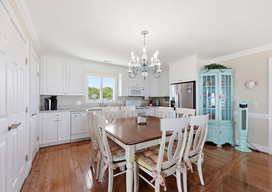 Gather around this spacious dining table in your bright, open kitchen—where white cabinetry, stainless appliances, and a charming chandelier create the perfect backdrop for your group's meals and morning coffee.