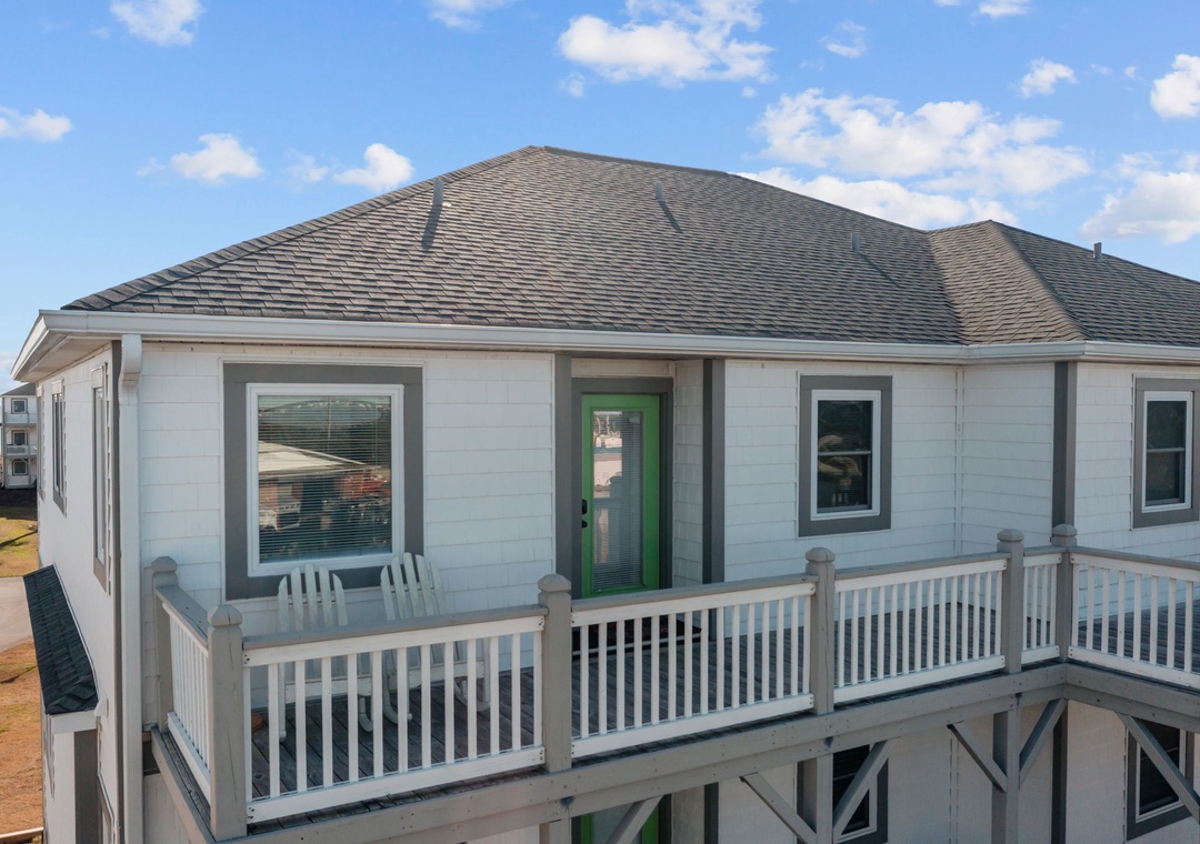 Charming beach house with wraparound deck overlooking scenic coastline, featuring bright green door and coastal charm.