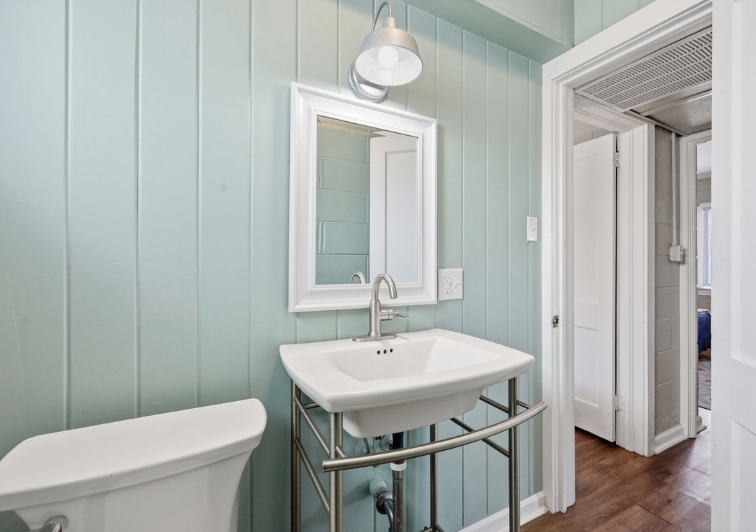 Step into your serene coastal-inspired bathroom with soft seafoam paneling, a classic pedestal sink, and warm hardwood floors that welcome you home after a day of exploring.