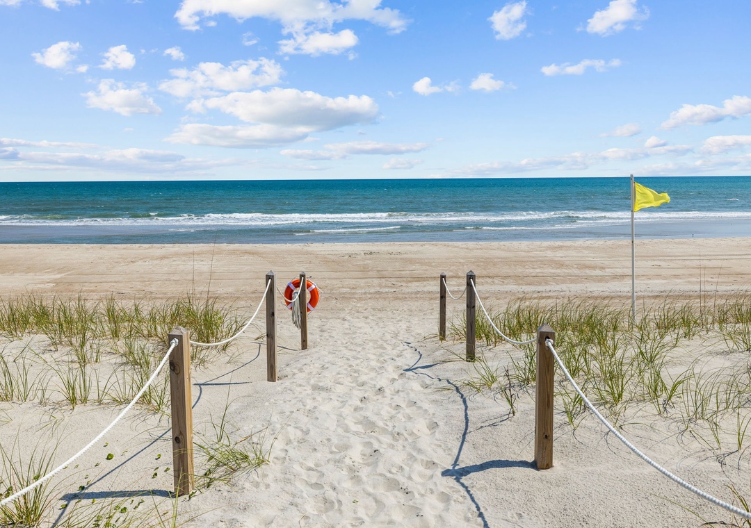 Pristine beach with protected dunes featuring wooden boardwalk access and safety flag for swimming conditions.