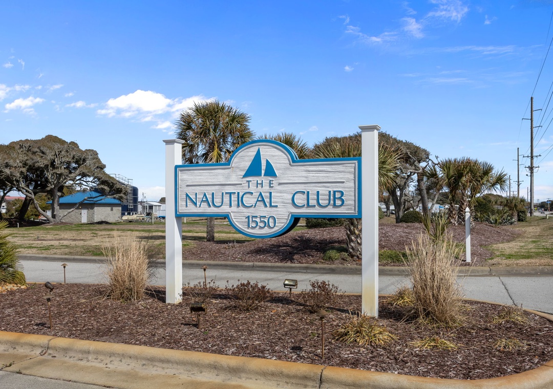 The Nautical Club property entrance sign welcomes guests to this coastal retreat surrounded by palm trees and natural landscaping.