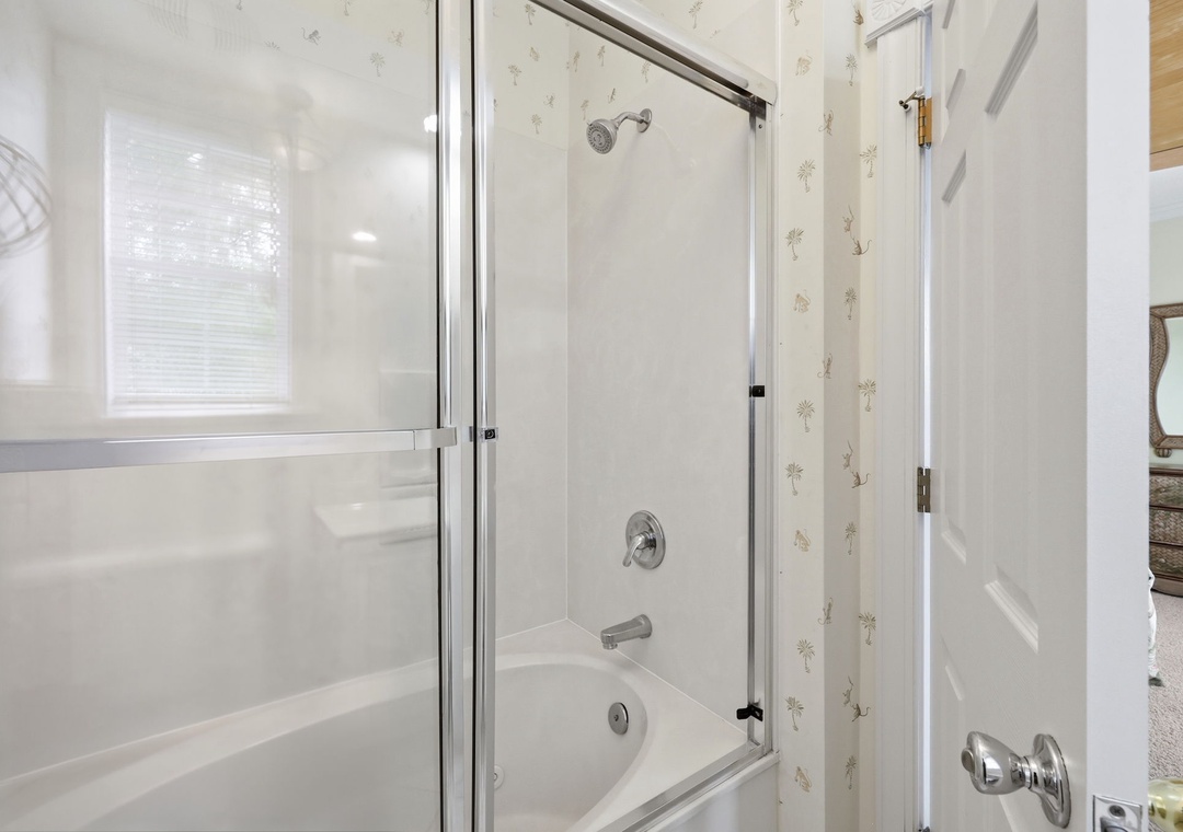 A bright, spotless bathroom with a tub-shower combo awaits your morning routine—glass doors, clean tiles, and natural light for a refreshing start.