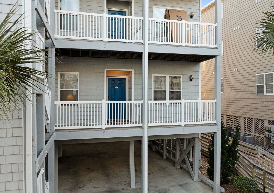 Multi-level beach house featuring white railings, blue door, and covered parking below.