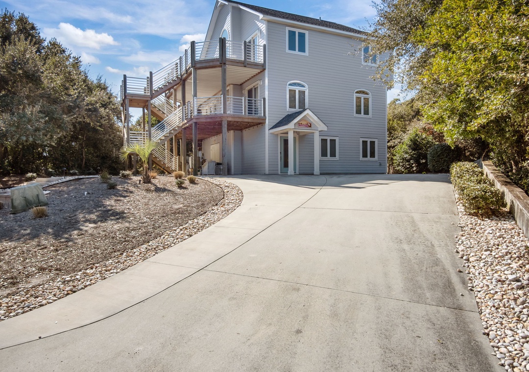 Spacious three-story coastal home with exterior stairs and private parking nestled among mature trees.