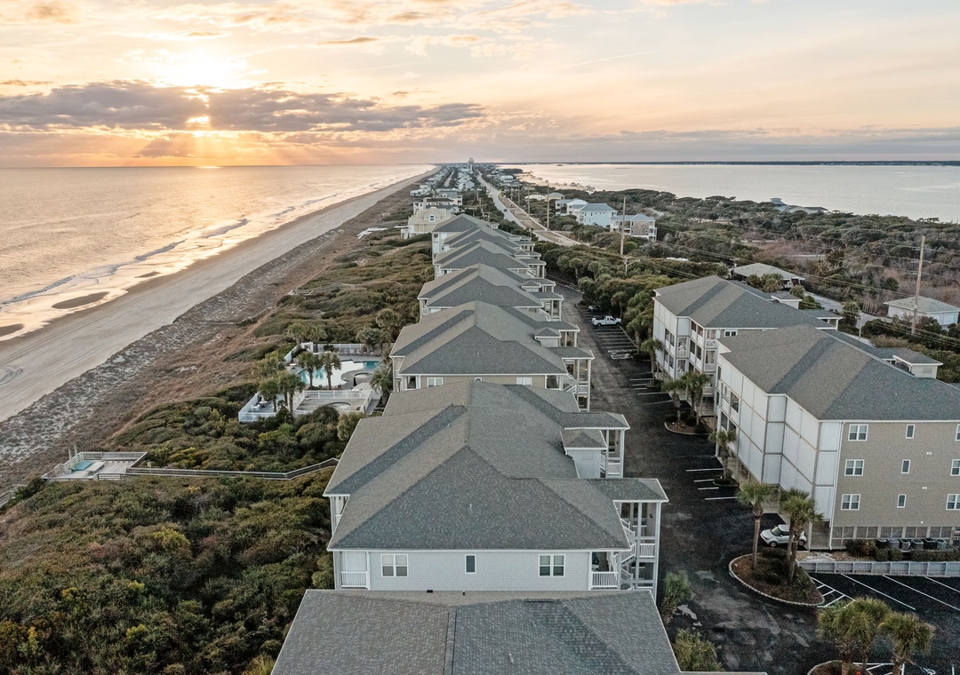 Aerial view of beachfront vacation rentals nestled along pristine coastline at sunset, offering direct beach access and ocean views.