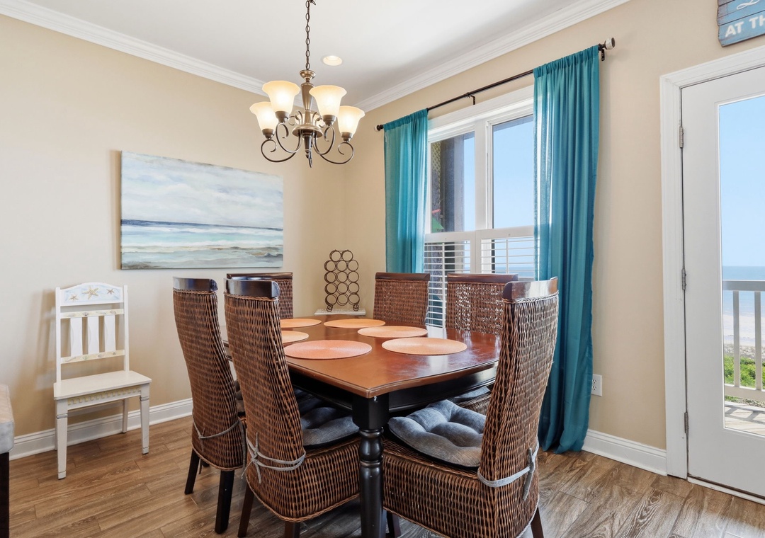 Picture yourself savoring meals at this inviting dining table, where coastal breezes drift through turquoise-draped windows and ocean views frame every bite. Warm wood tones and woven textures create a relaxing space for gathering.