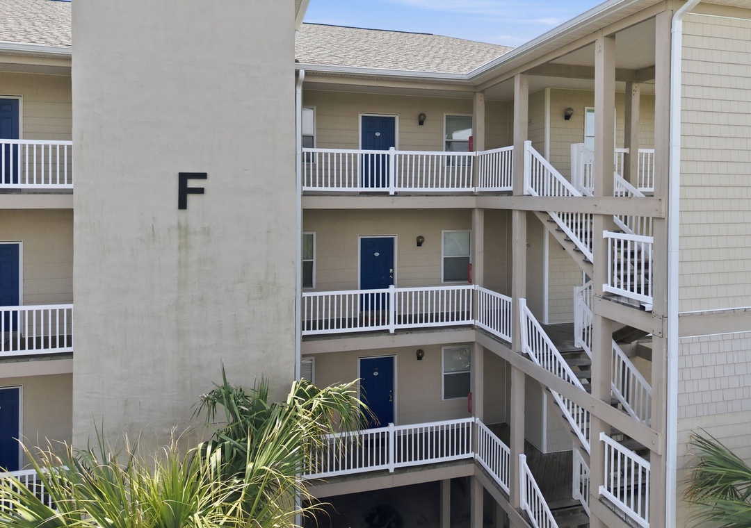 A multi-level beachside building with bright white balconies and blue doors marking each unit entrance, offering easy access and coastal charm.