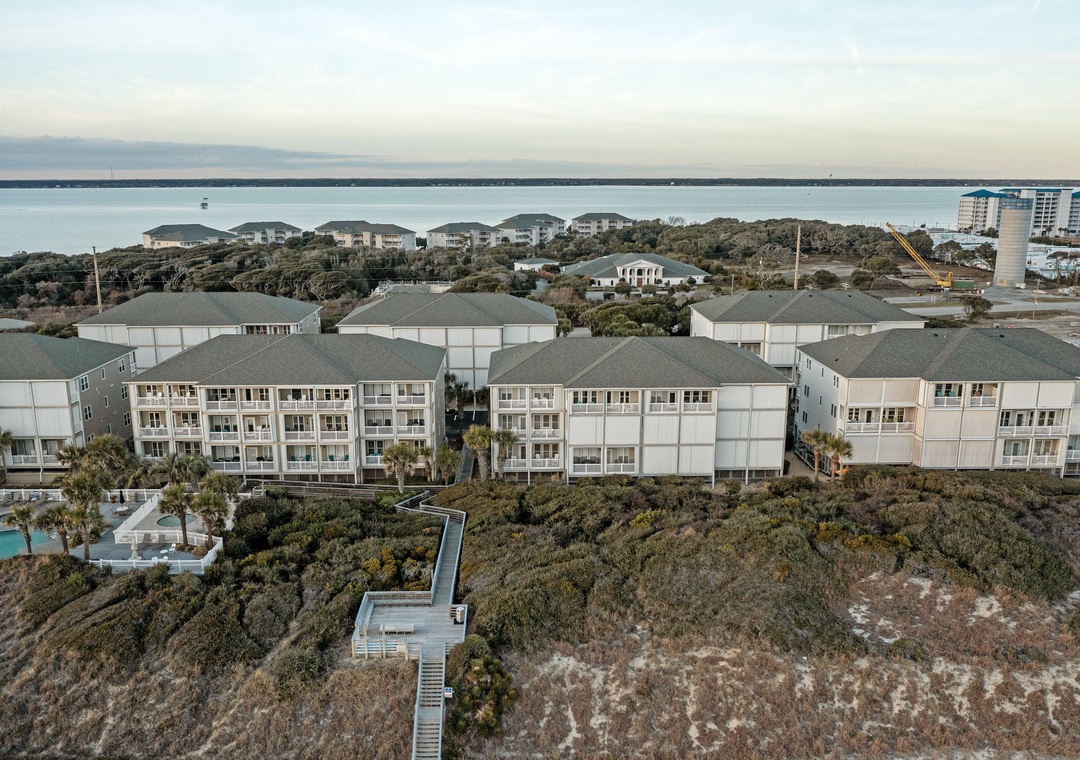 Coastal resort buildings nestled among natural dunes with ocean views and beach access via elevated walkway.