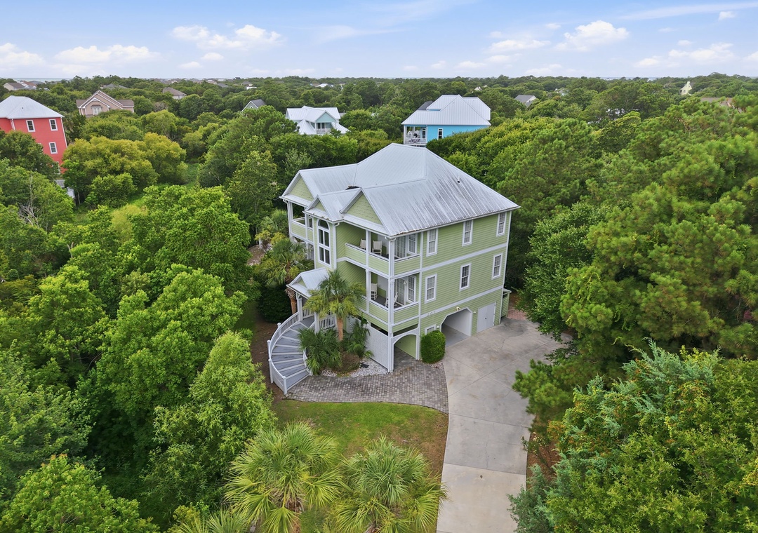 A spacious three-story coastal home nestled among lush greenery, featuring a covered entrance, ample parking, and a peaceful neighborhood setting with nearby beach access.