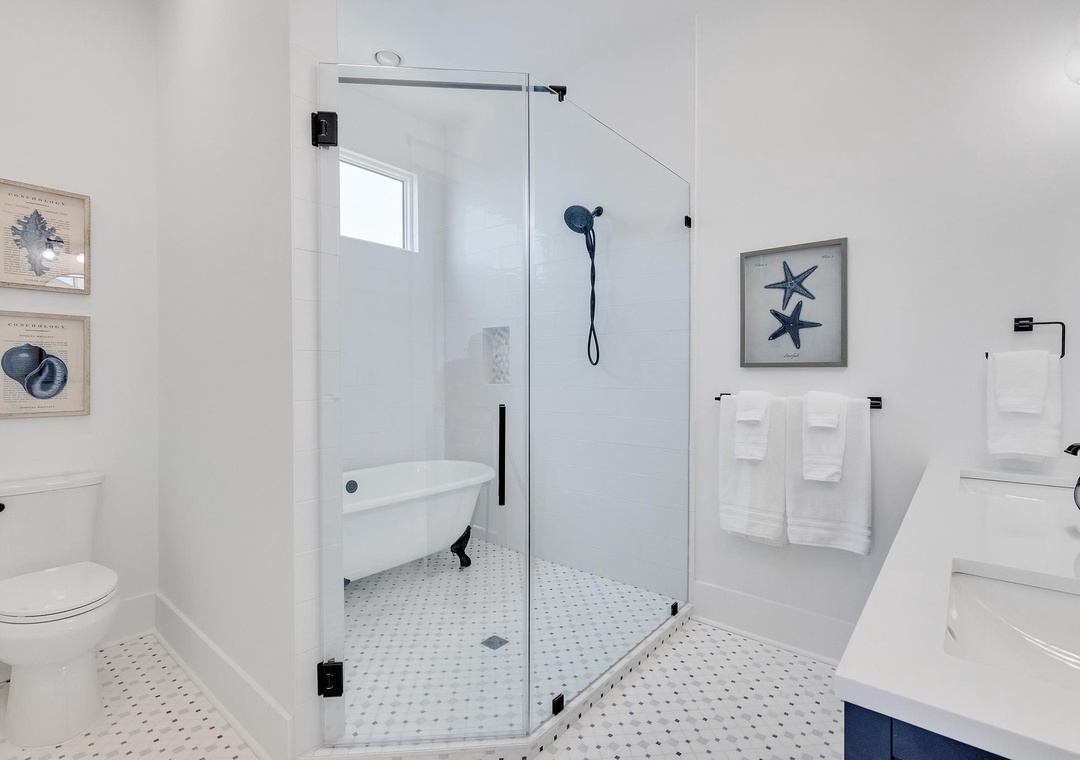Refresh in your spa-like bathroom with a spacious glass-enclosed shower and vintage clawfoot tub. Crisp white towels and coastal artwork create a serene retreat.