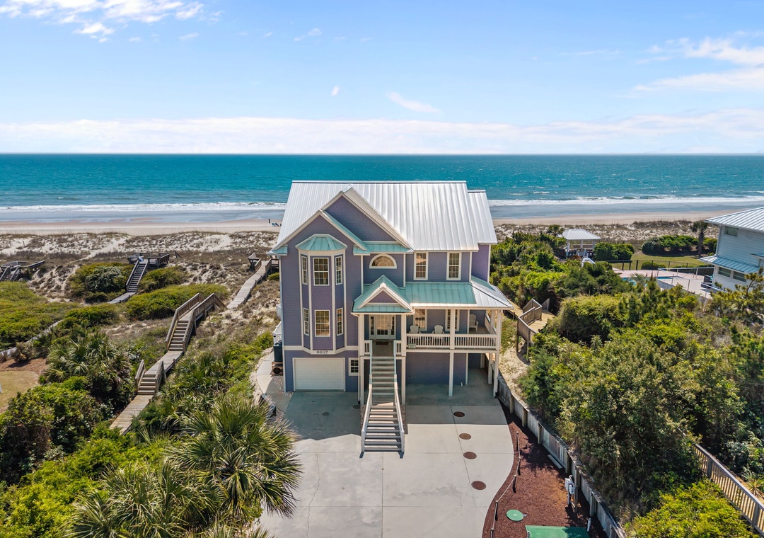 Stunning beachfront home with direct beach access, surrounded by lush coastal vegetation and pristine sandy shores.