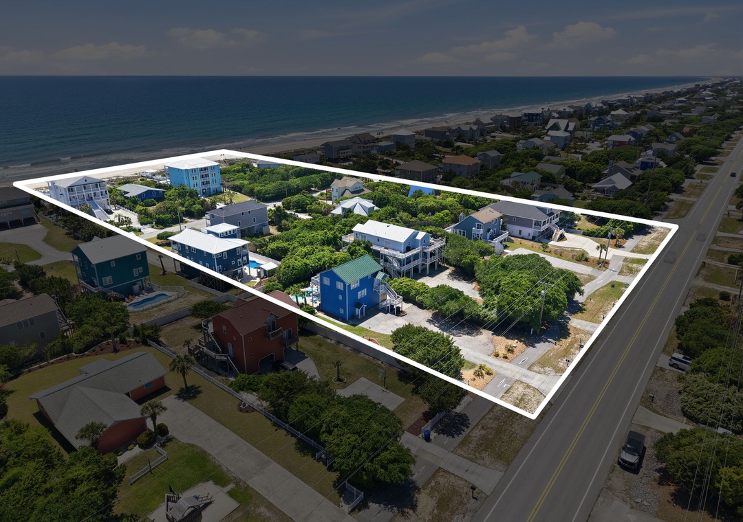 Aerial view of a beachfront property area featuring multiple vacation homes nestled among coastal greenery, with direct beach access and ocean proximity in a residential neighborhood.