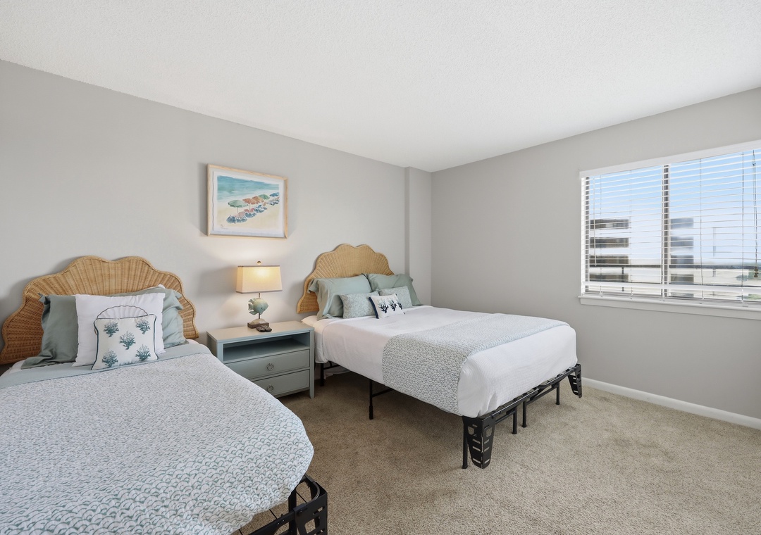 Your bright, coastal-inspired bedroom features two plush beds with natural wicker headboards and soft linens. Wake to natural light streaming through your window, with charming beach-themed decor adding a serene, beachy ambiance.