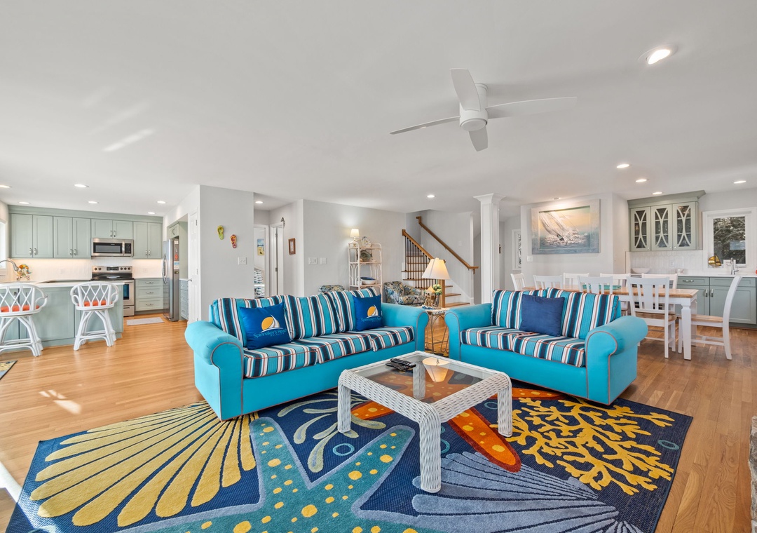 Relax in your vibrant open-concept living space with cheerful blue sofas, coastal-themed decor, and a fully equipped kitchen perfect for family gatherings.