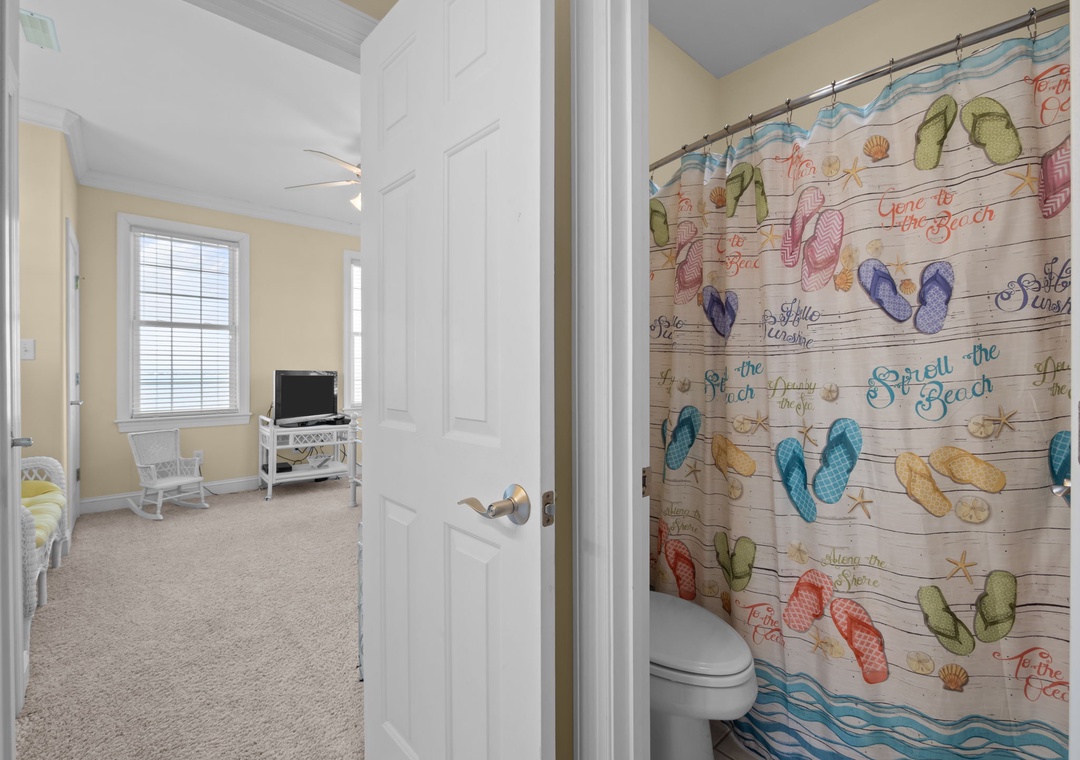 Your private bathroom features a whimsical beach-themed shower curtain, while your cozy bedroom awaits with comfortable seating and entertainment nearby.