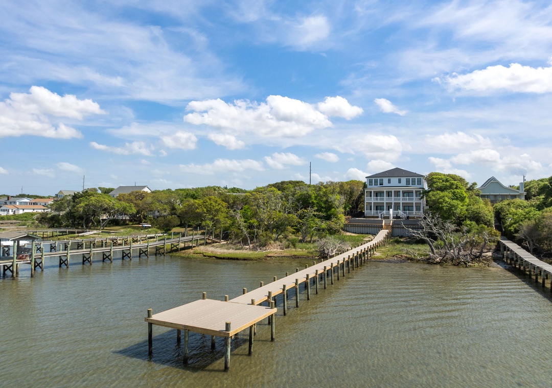 Stunning waterfront property with private dock stretches into calm waters, surrounded by lush coastal landscape and blue skies.