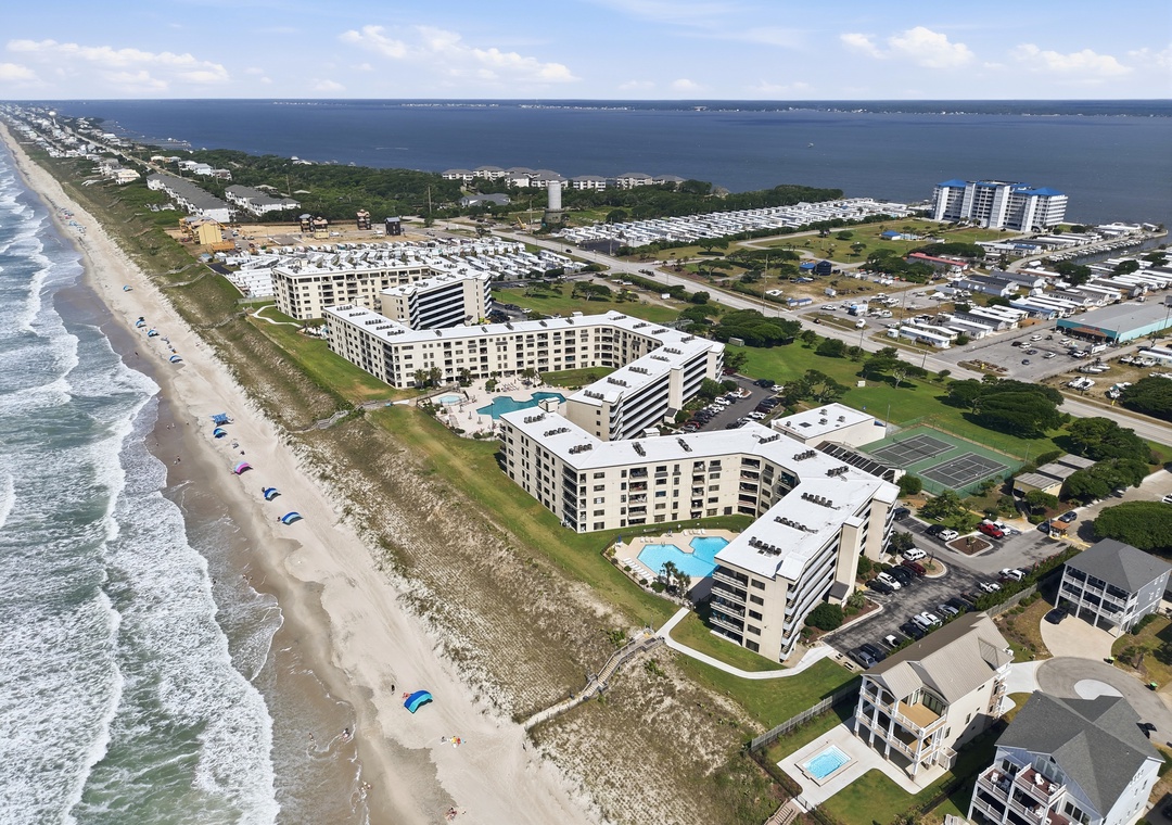 Beachfront vacation rental complex featuring multiple buildings, swimming pools, and tennis courts, with direct beach access along the Atlantic coastline and waterway views.