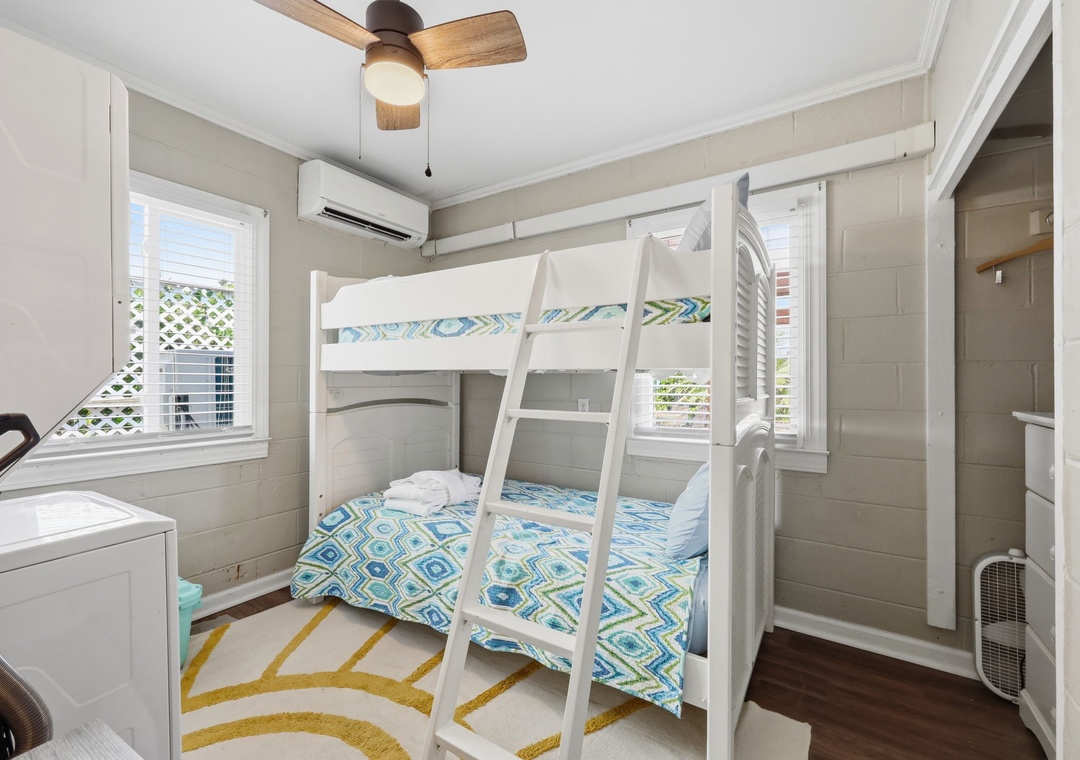 Your coastal-chic bunkroom offers a cheerful retreat with bright white shiplap, vibrant bedding, and a ceiling fan to keep you cool. Large windows flood the space with natural light, while the AC ensures comfort.
