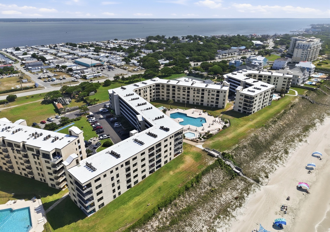 Beachfront resort complex featuring modern buildings, swimming pool, and convenient access to sandy shores along a scenic coastal area.