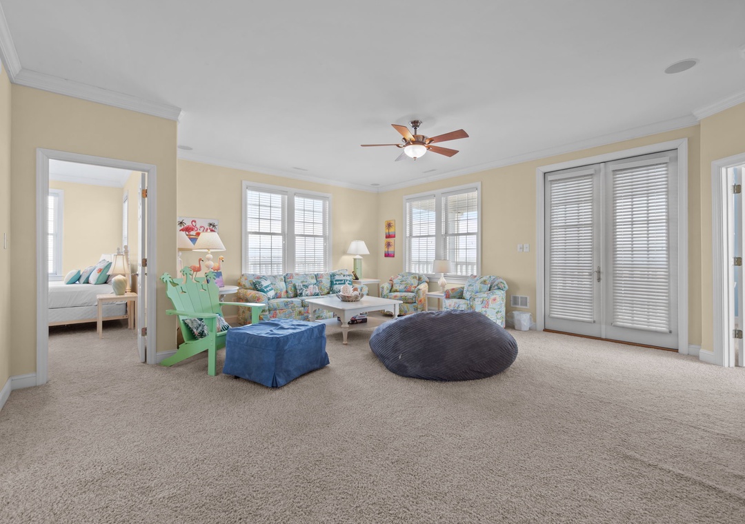 Relax in your spacious living room featuring coastal-themed seating, a cozy bean bag, and bright windows that fill the space with natural light.