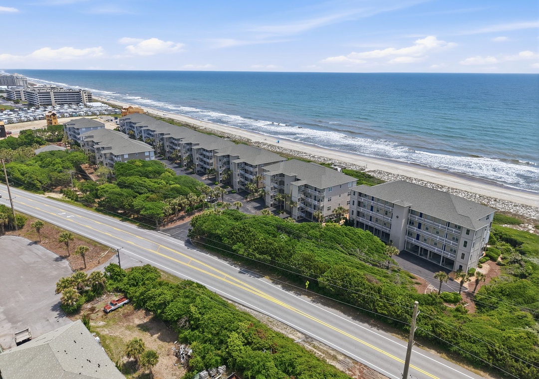 Aerial view of beachfront property nestled between coastal road and pristine sandy shore, offering direct beach access and stunning ocean views along a serene stretch of coastline.