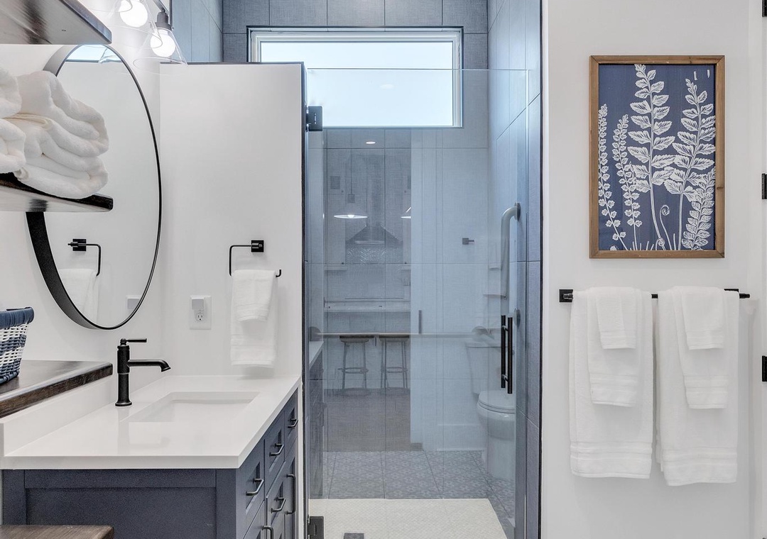 Your private bathroom blends modern elegance with spa-like serenity. Crisp white cabinetry, patterned tile floors, soft towels, and a sleek glass-enclosed shower invite you to unwind.