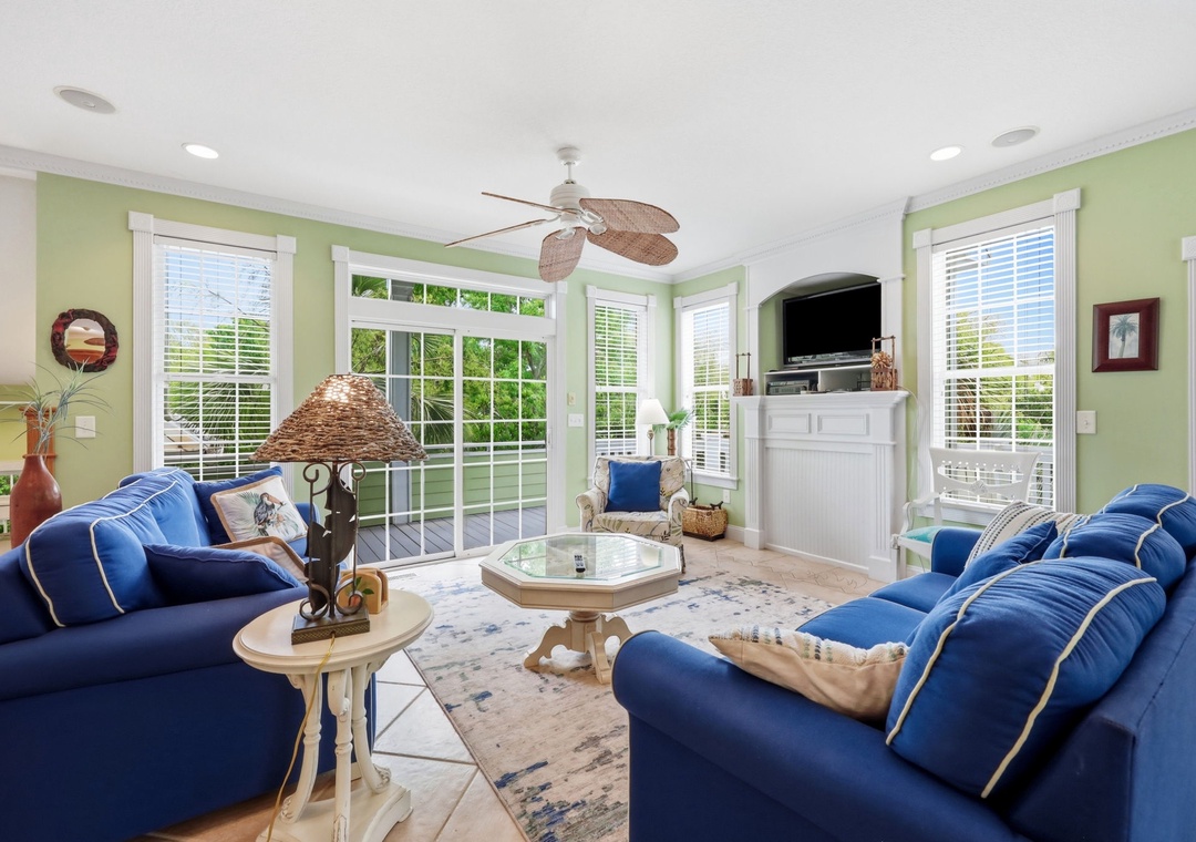 Sink into plush blue sofas beneath a breezy ceiling fan as natural light pours through French doors. Your coastal-chic living room invites relaxed evenings with garden views and modern entertainment.