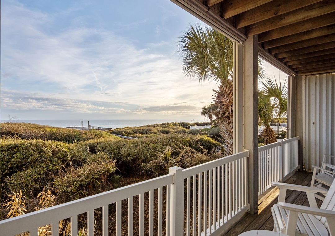 Covered deck with coastal views featuring natural dunes, palm trees, and distant water glimpses through tropical vegetation.