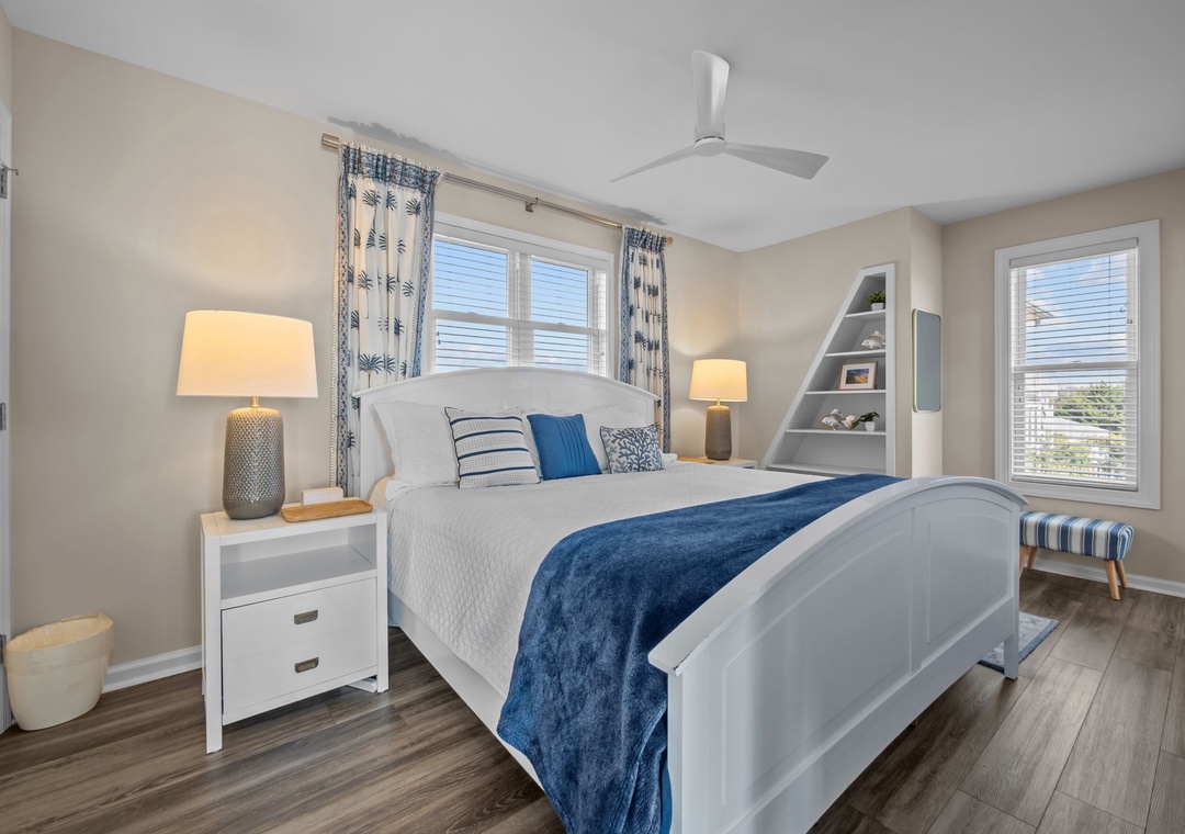 Unwind in your peaceful bedroom sanctuary with coastal-inspired blues, warm lamps, and a ceiling fan for ultimate comfort.