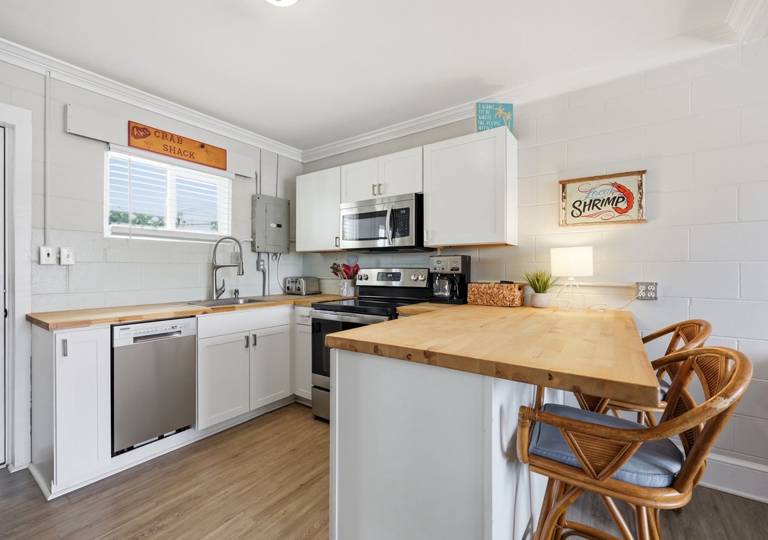 Your fully equipped kitchen features warm wood countertops, modern appliances, and a cozy breakfast bar with rattan stools—perfect for preparing meals and sharing stories over morning coffee.