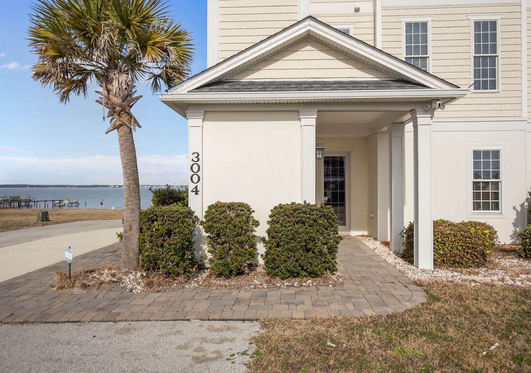 Charming waterfront property entrance with coastal landscaping and scenic bay views in the background.