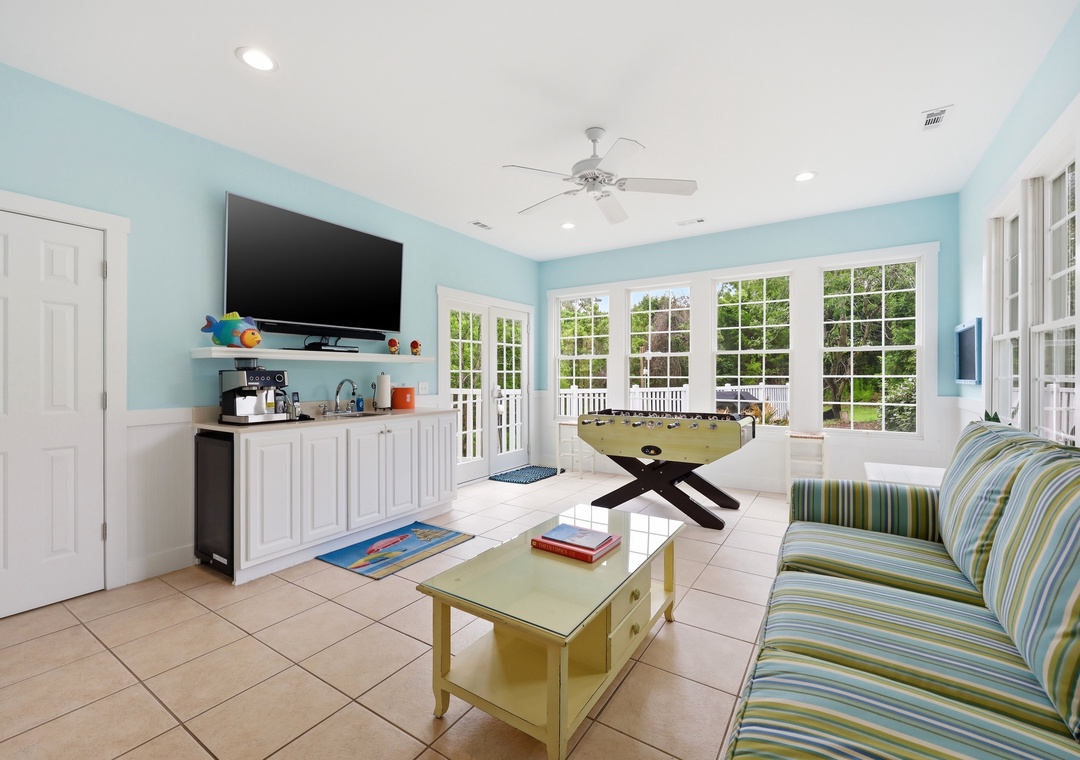 Unwind in your cheerful coastal lounge with comfy seating, entertainment center, and a foosball table for friendly competition. French doors open to the garden, flooding the space with natural light and fresh air.