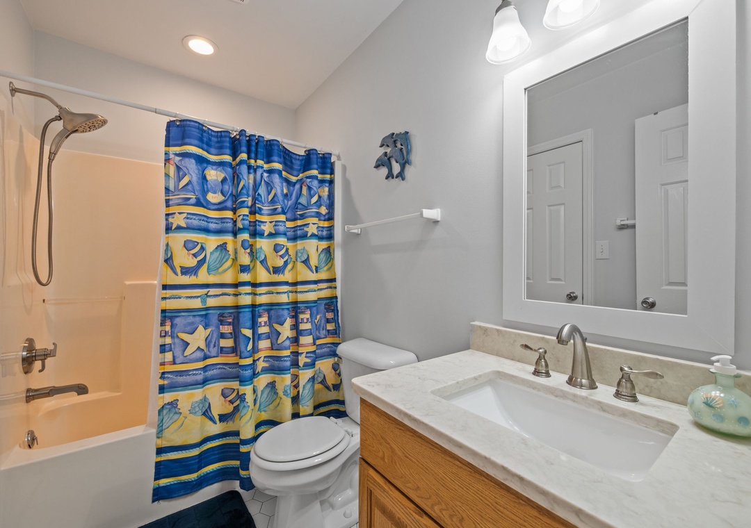 Your private bathroom features a tub-shower combo with cheerful ocean-themed curtain, creating a bright coastal vibe for your refreshing retreat.
