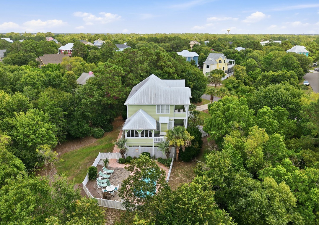 Aerial view of a charming coastal vacation rental nestled among lush greenery in a peaceful residential neighborhood, featuring a private patio and outdoor seating area.