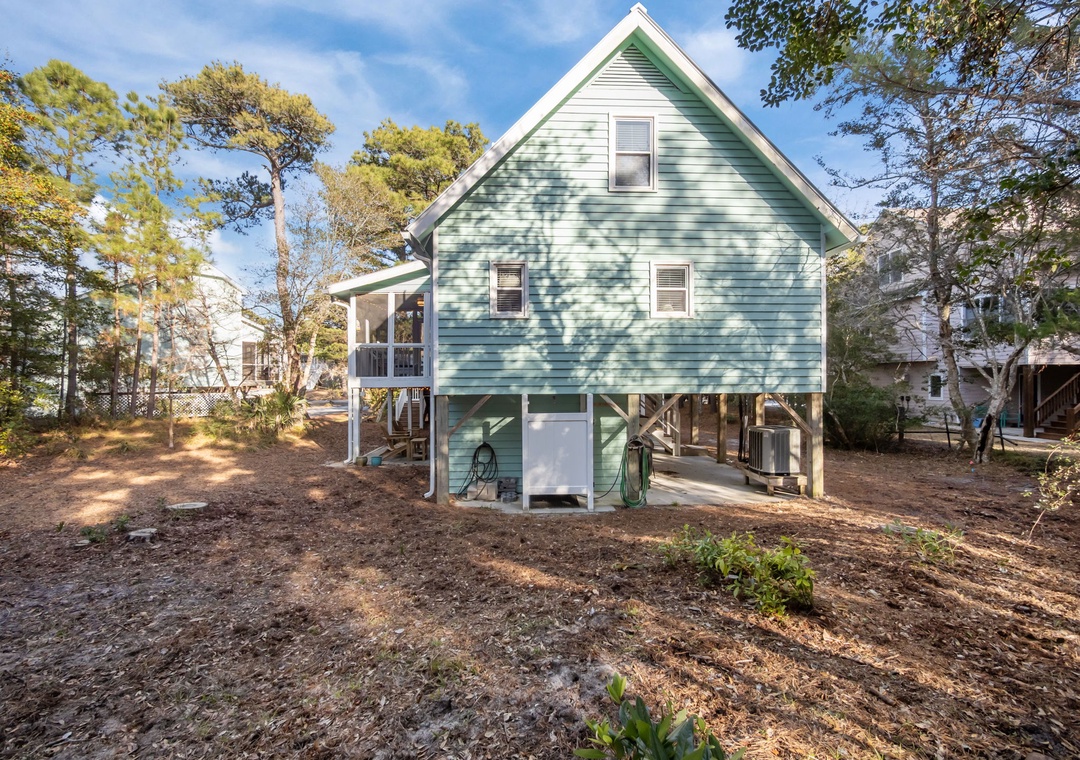 Charming coastal cottage with elevated design and enclosed parking sits among mature trees in a peaceful neighborhood setting.