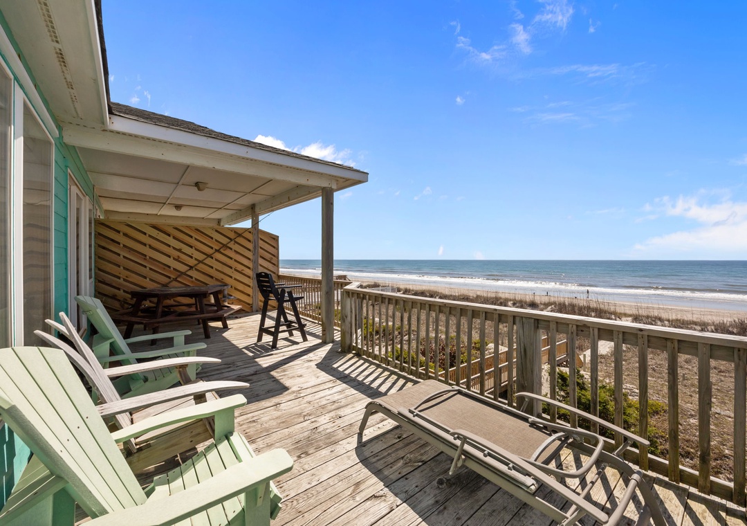 Beachfront deck with Adirondack chairs and dining table overlooking pristine sandy shores and endless ocean views.