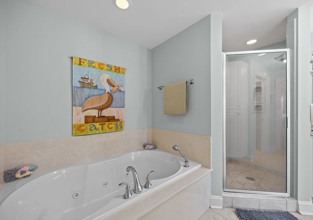 Unwind in your spa-like bathroom with a deep soaking tub and separate glass shower, complete with coastal artwork.