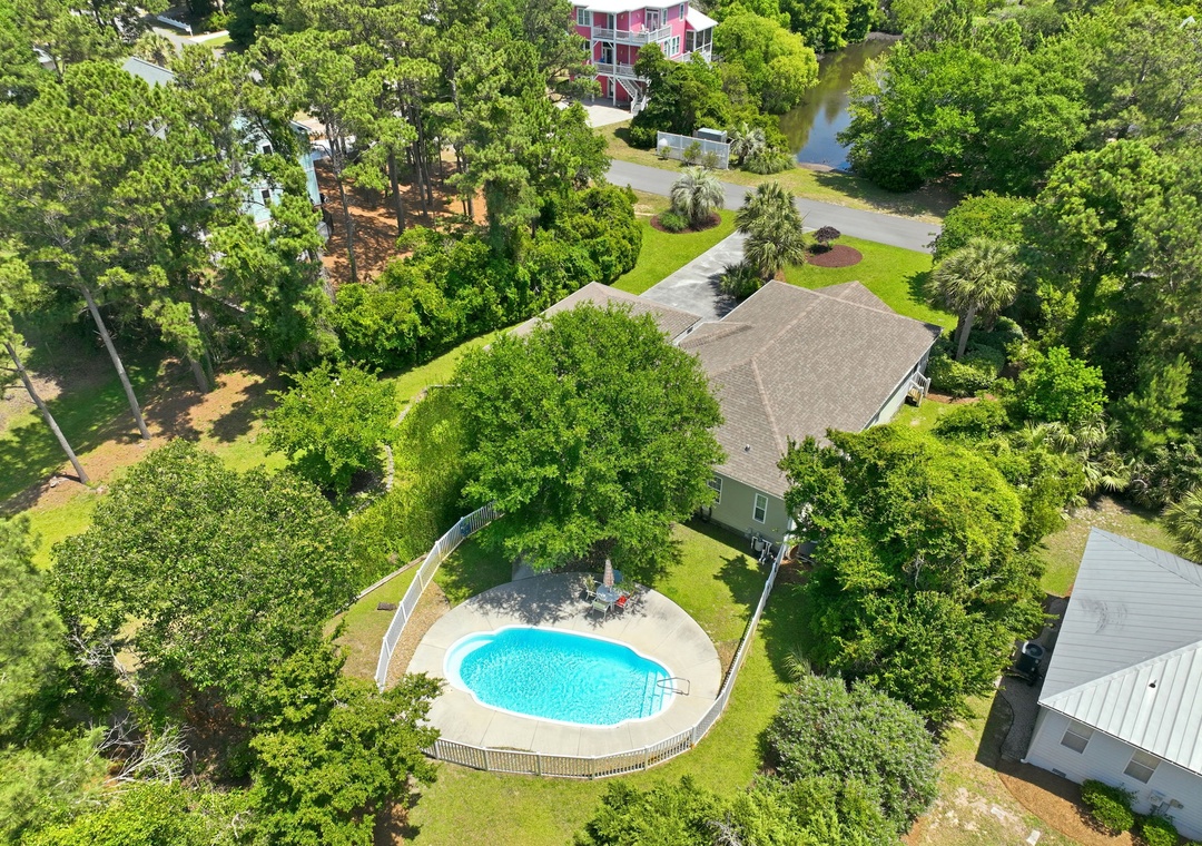 Aerial view of a serene rental home featuring a private backyard pool nestled among lush greenery and mature trees in a peaceful residential neighborhood.
