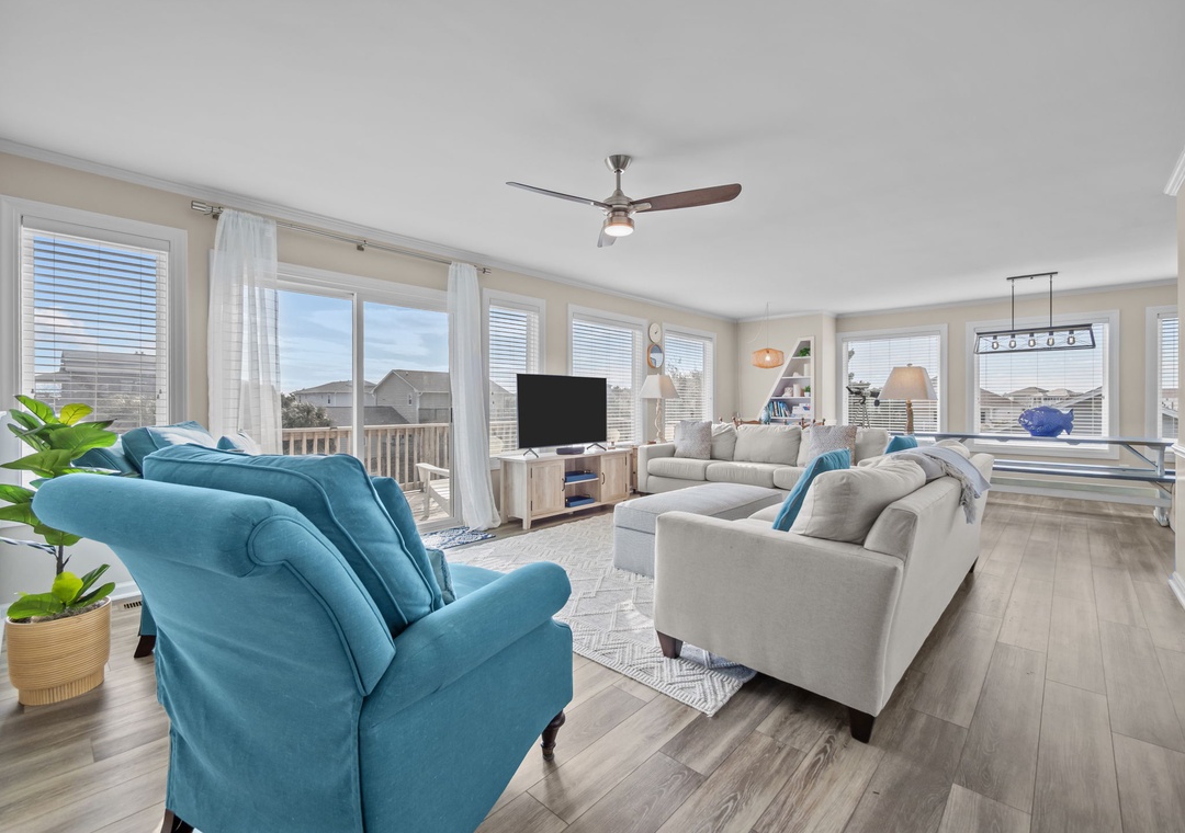 Relax in your spacious living room with plush seating, modern TV, and abundant natural light from large windows.