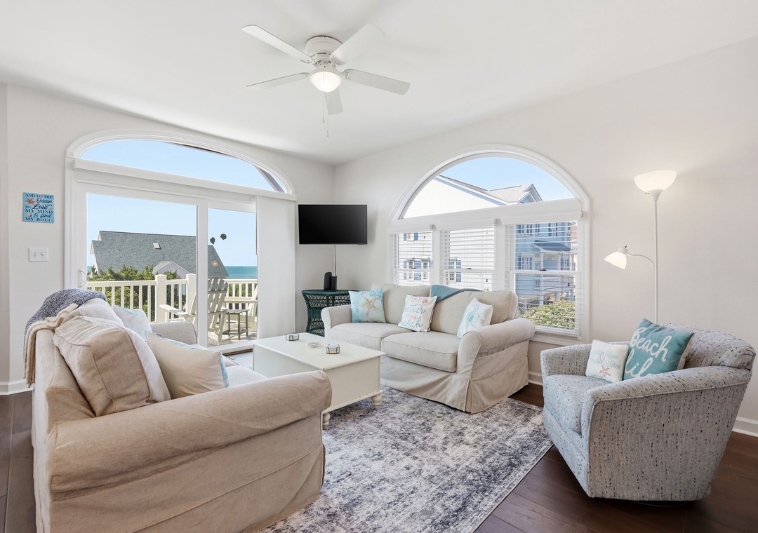Unwind in your coastal sanctuary, where soft neutral tones meet ocean breezes. Picture yourself on plush seating, ocean views framed by elegant arched windows, ceiling fan spinning gently overhead.